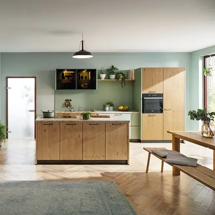 Küche mit Holzfronten, Kochinsel, Hochschrank, Sitzbank und Tisch an grüner Wand